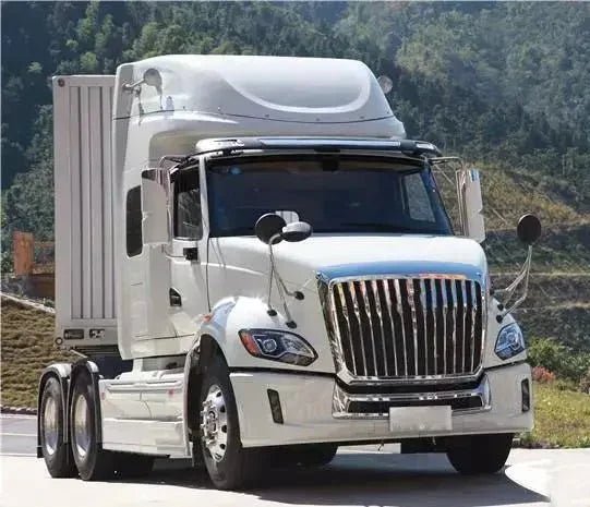 White semi truck with chrome grille parked outdoors near green hills under a clear sky
